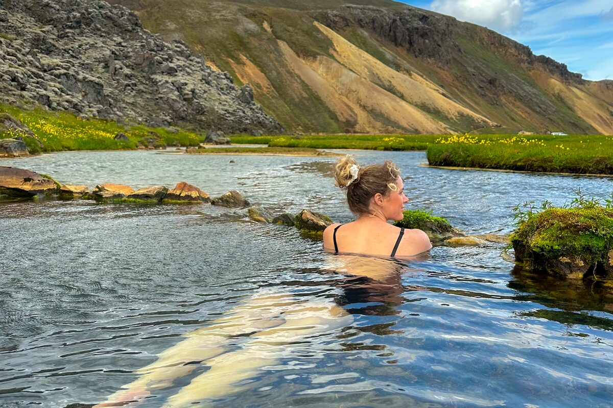 Female laying in hot springs at Landmannalaugar baths in camp site by huts.