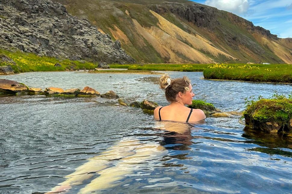 Female laying in hot springs at Landmannalaugar baths in camp site by huts.