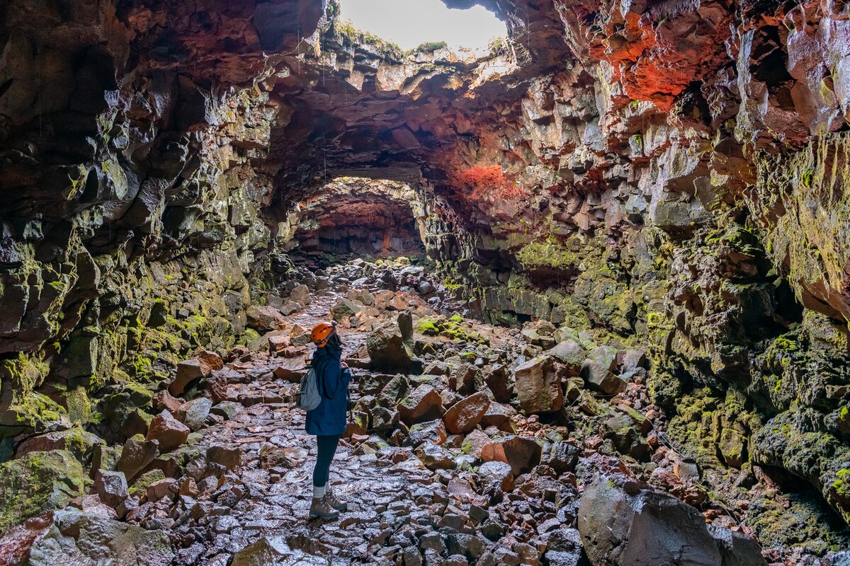 Tourist looking up to light shining from above into lava tunnel entrance