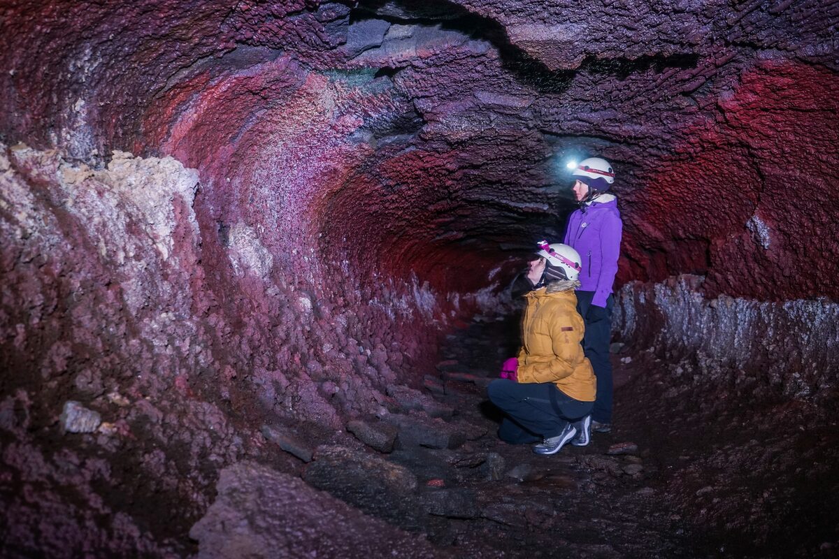 Tourists crouching down using safety helmet torch to view lava tunnel walls up close