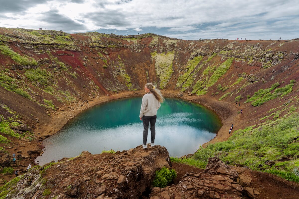 Young female standing at edge of Kerid volcanic crater lake in Spring time 