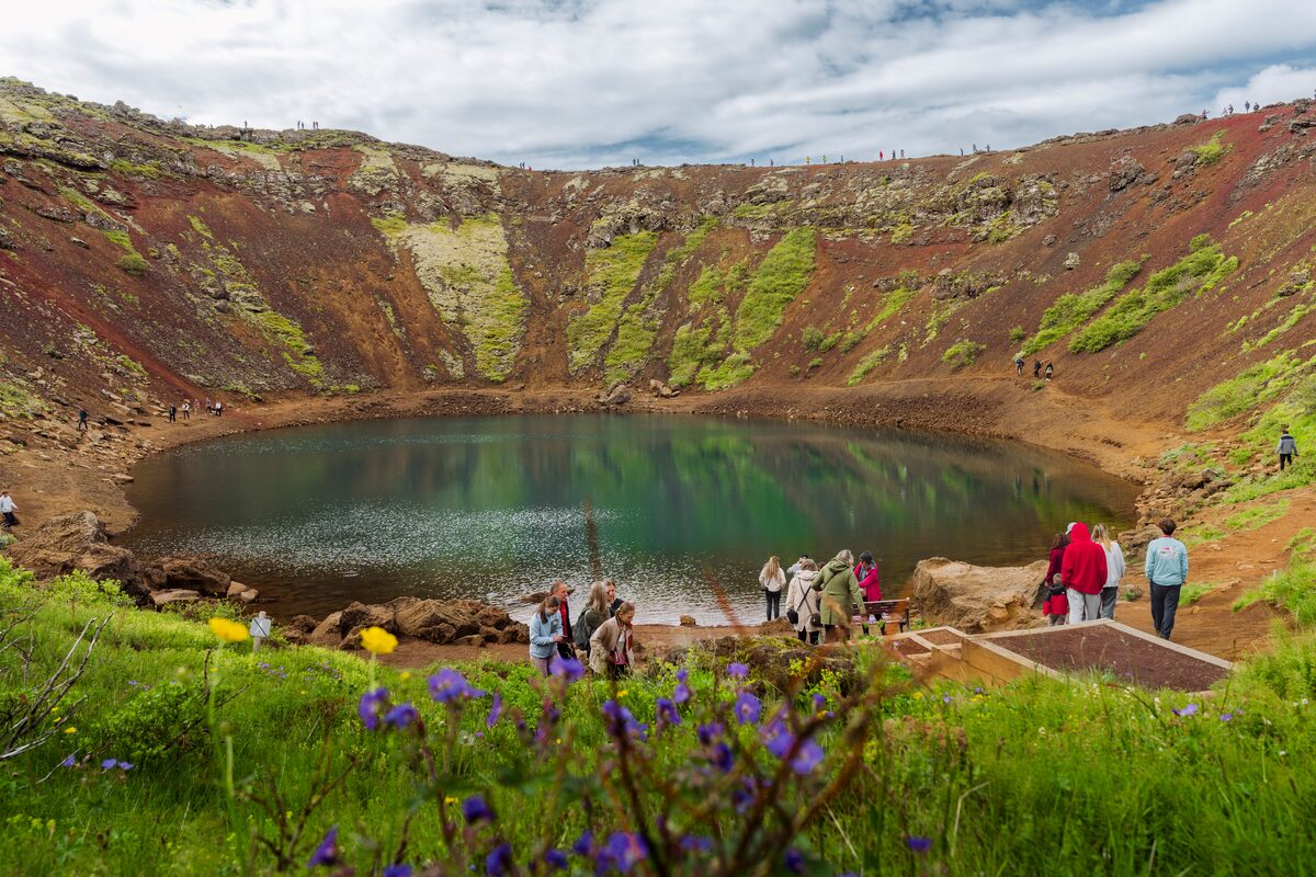 Small group tour at bottom of kerid standing by lake next to flowers blossoming 