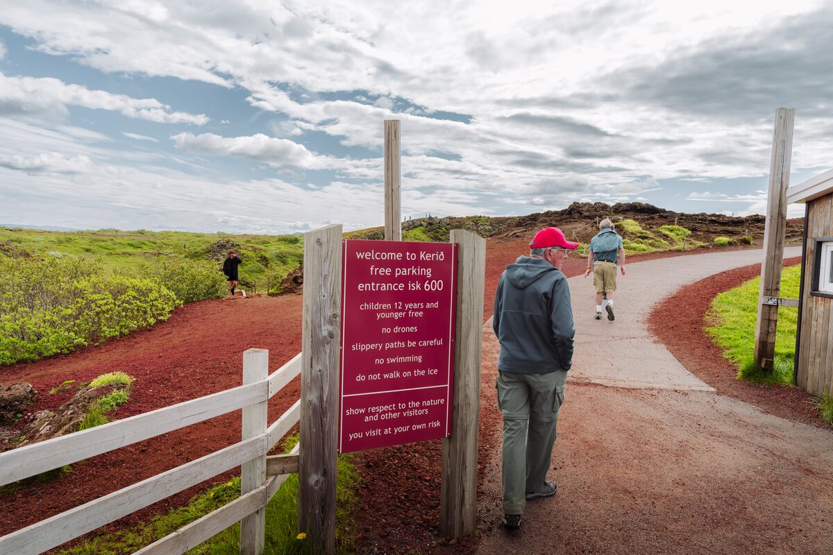 Tourist walking past price sign at Kerid Crater entrance to view point