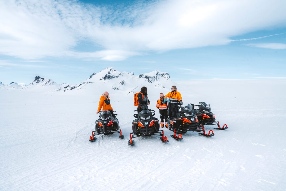 Small group of people on snowmobiling posing for photo in front of Langjokull glacier