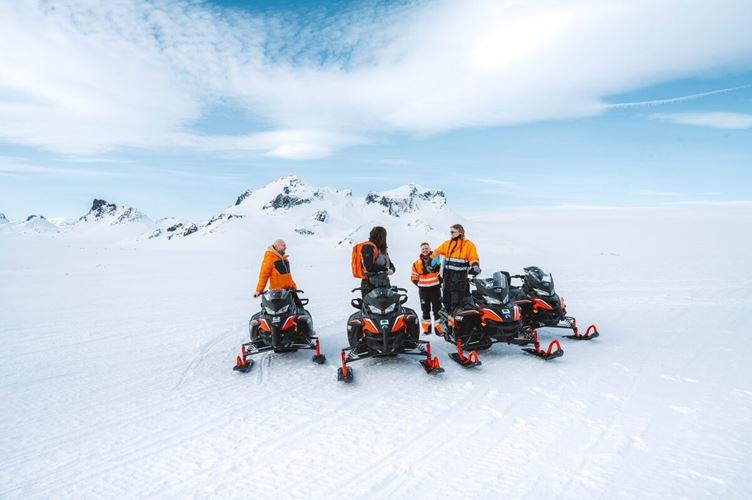 Small group of people on snowmobiling posing for photo in front of Langjokull glacier