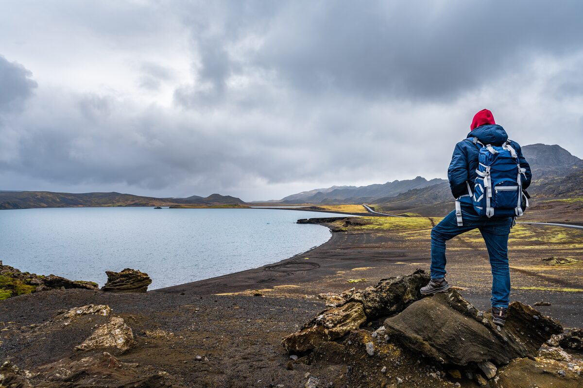 Tourist with backpack standing on rock formation peak by Kleifarvatn lake.