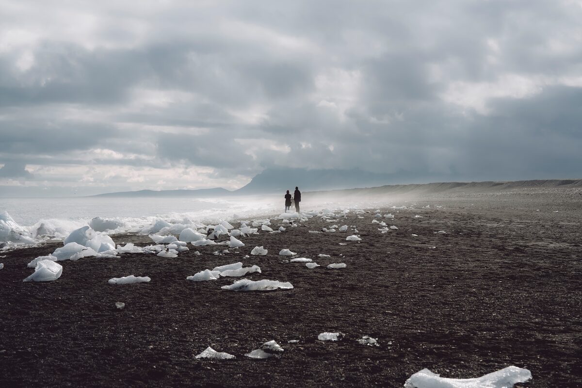 Couple standind together looking out to sea, at Diamond beach covered in Jokulsarlon's ice bergs.