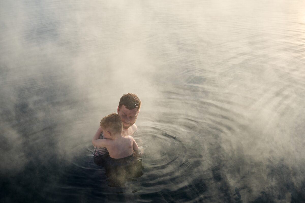 Father and baby bathing in Secret Lagoon during sunset in summer.