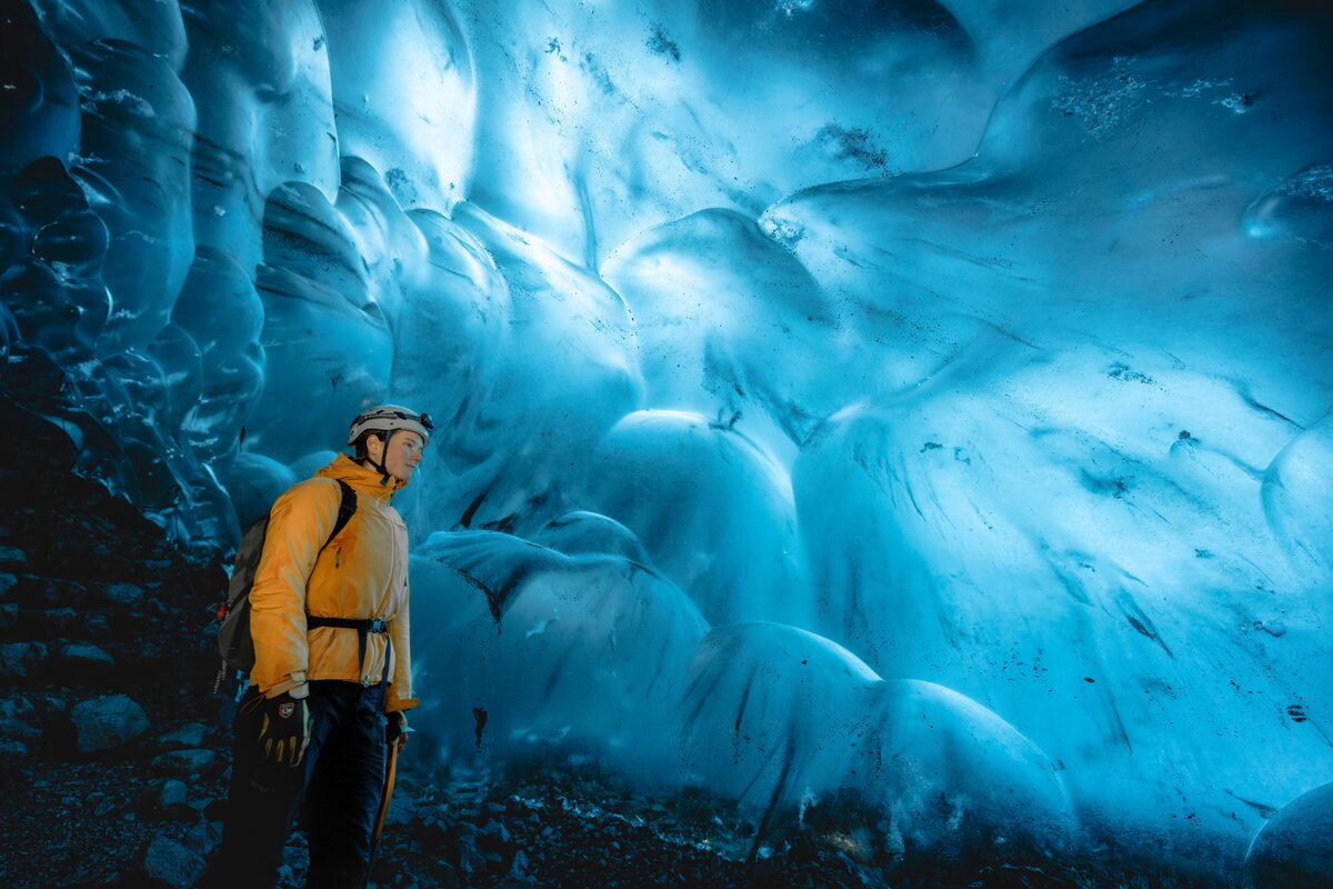 Male in yellow coast and safety helmet inside blue ice cave in Iceland.