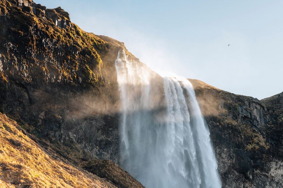 Sunset sets over Seljalandsfoss waterfall reflecting over waterfalls mist.