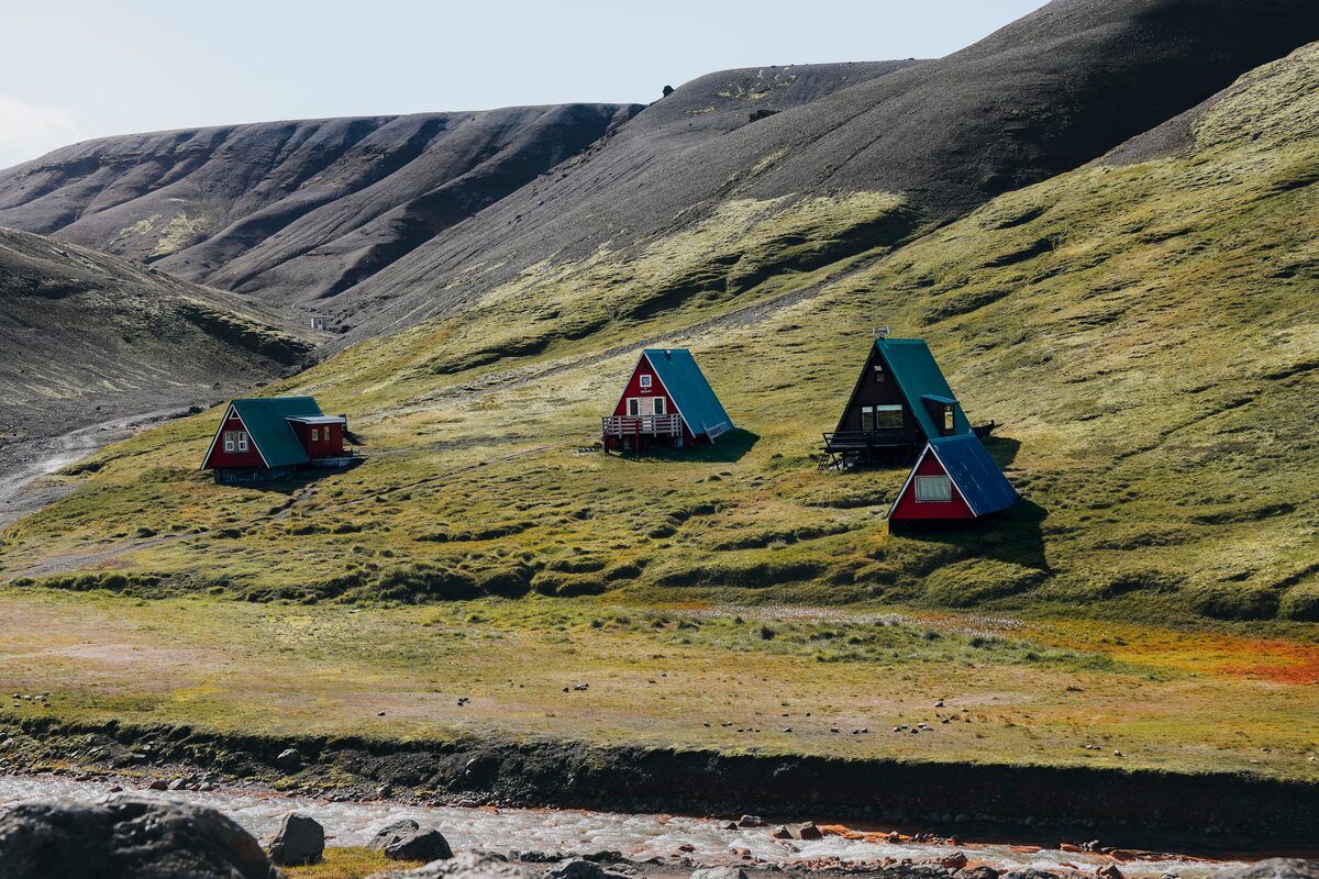 Red, triangle Highland Base cabins among hills near the Ásgarður River.