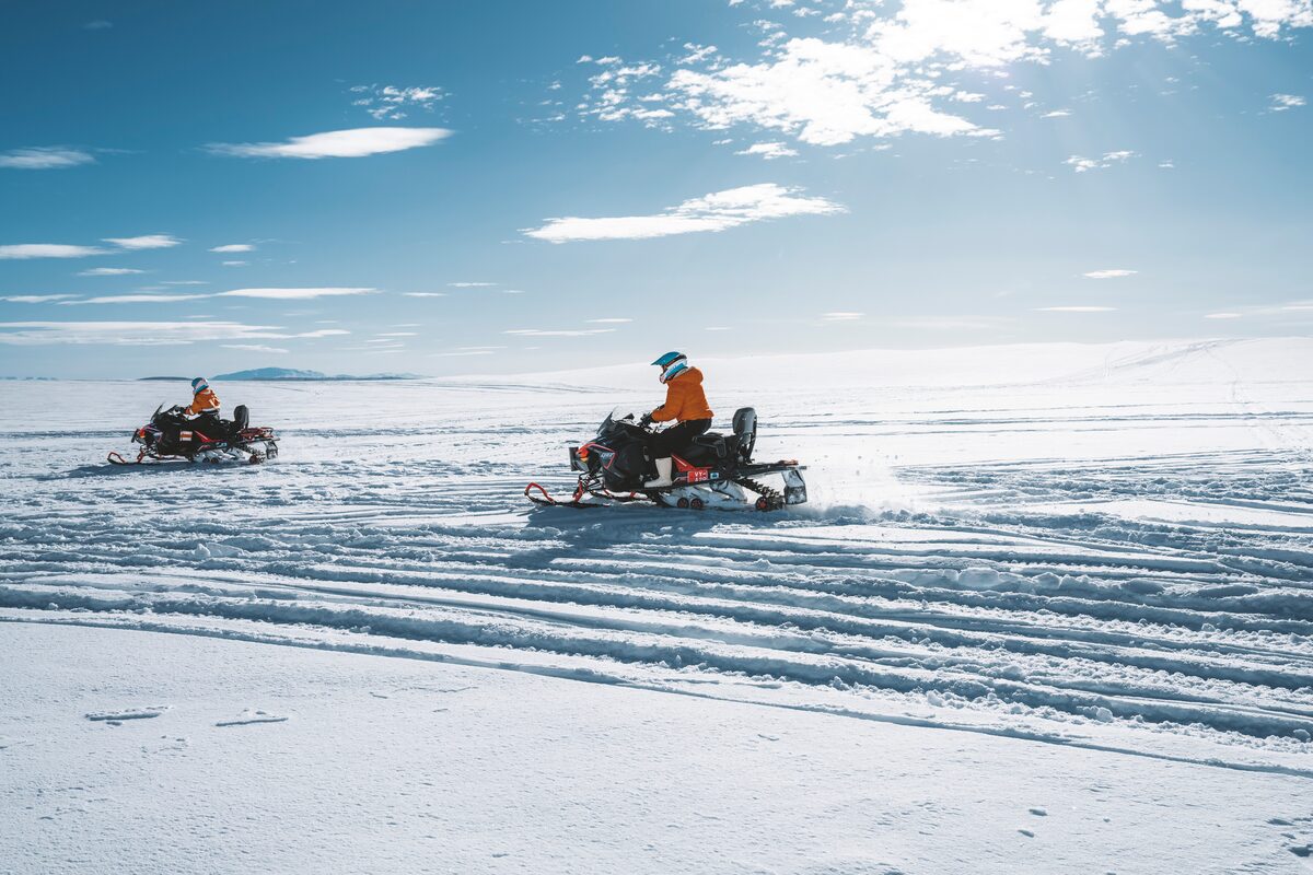Two people riding snowmobiles leaving tracks on snow at Langjokull glacier.