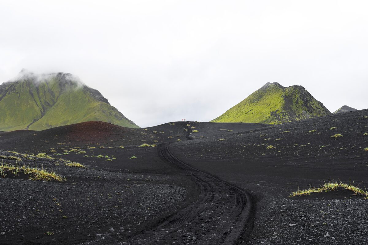 Black volcanic sand covered floor and small hiking group in distance by moss covered mountains at Emstrur.