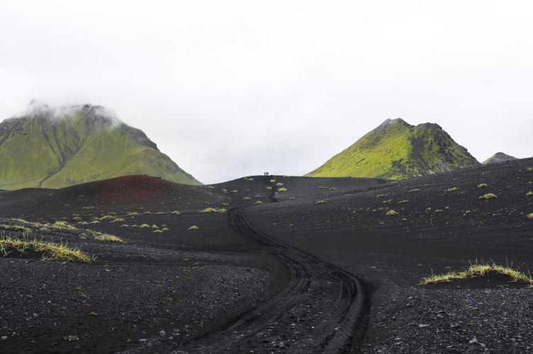 Black volcanic sand covered floor and small hiking group in distance by moss covered mountains at Emstrur.