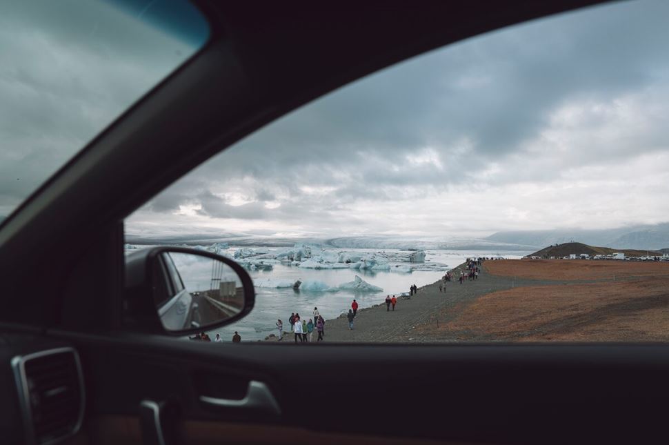 A view of tourists walking close to icebergs at Jokulsarlon glacier lagoon shore from car window.
