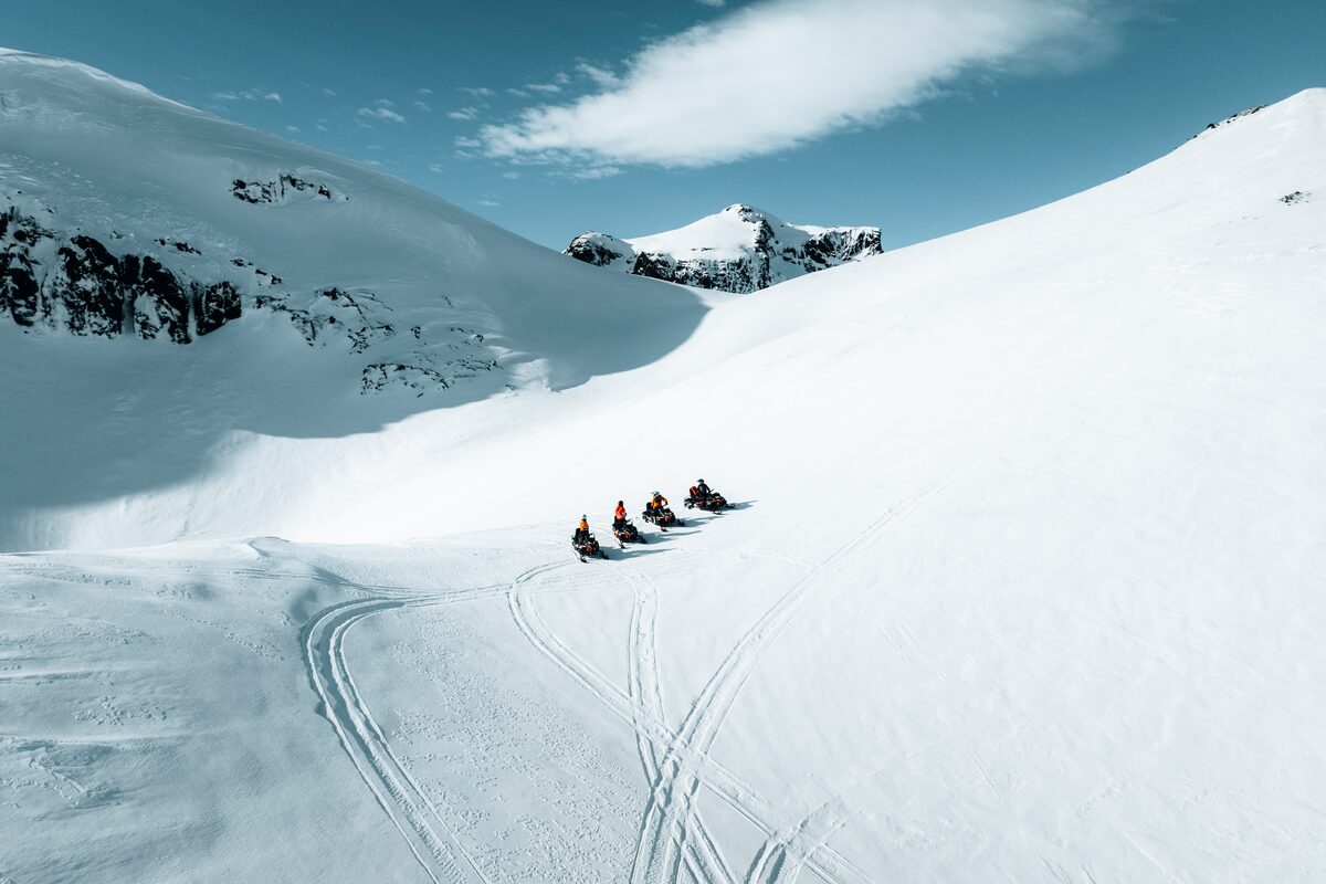 Four snowmobilers parked in a row on Langjokull glacier slant during summer.
