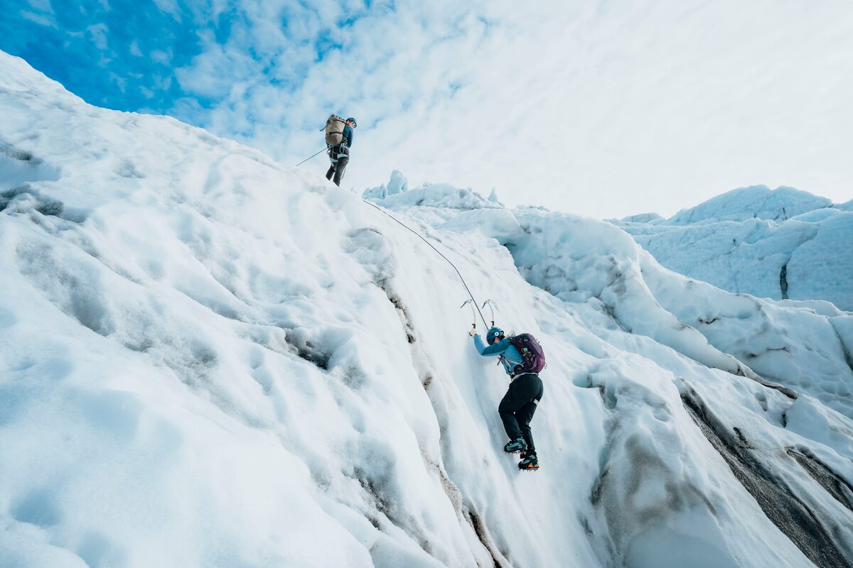 Ice climbing duo at large ice crevasse on glacier, using ice picks.