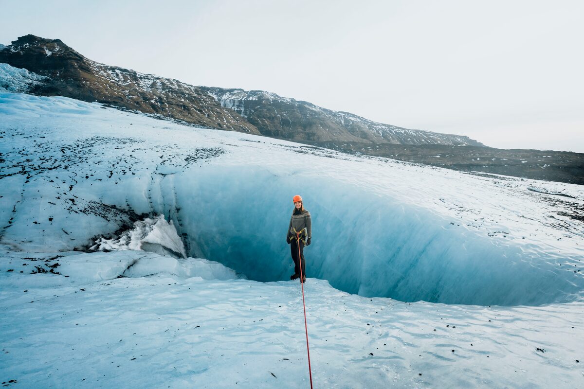 Tourist standing on large blue ice crevasse at Vatnajokull glacier.