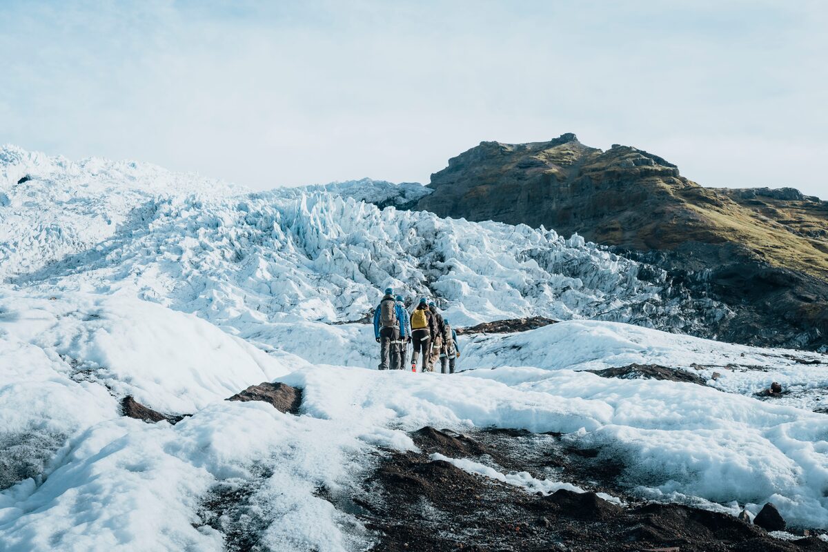 Small group of tourists wearing safety gear hiking across Vatnajokull landscape.
