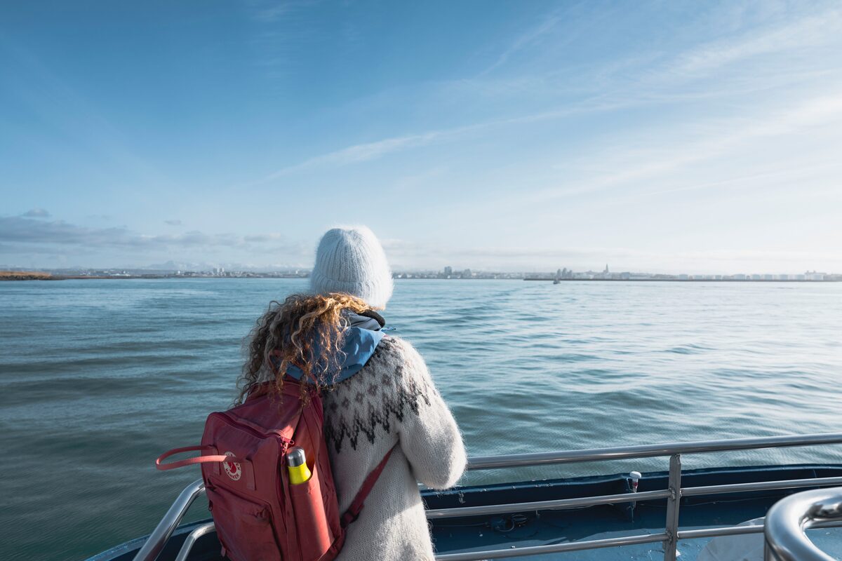 Young female dressed in Icelandic Jumper watching out to ocean from boat.