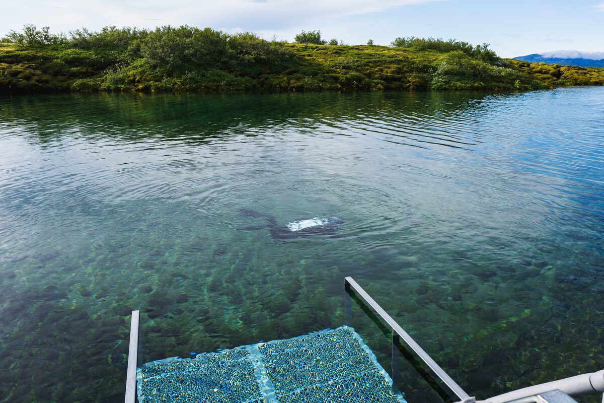 View from above Silfra waters of a person snorkeling in the clear waters.