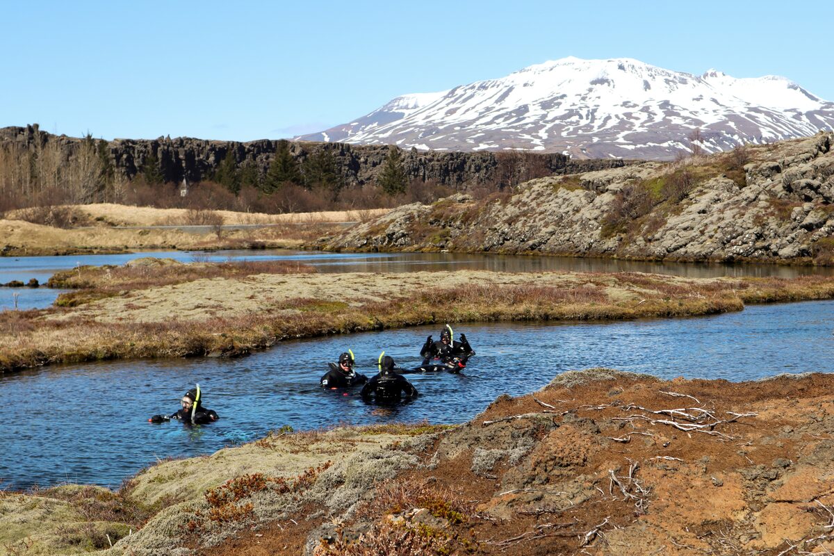 Group of people snorkeling at Silfra Fissure in autumn, views of snowy mountain in distance.