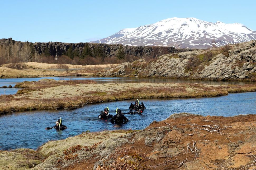 Group of people snorkeling at Silfra Fissure in autumn, views of snowy mountain in distance.