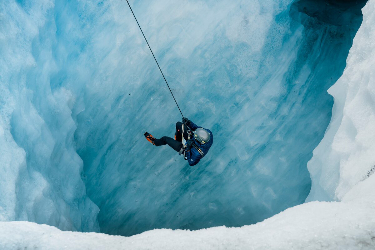 Male suspended with rope down blue ice wall at Solheimajokull glacier.