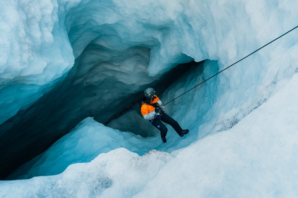 Male attached to climbing rope climb steep deep blue ice crevasse at Solheimajokull in Iceland.