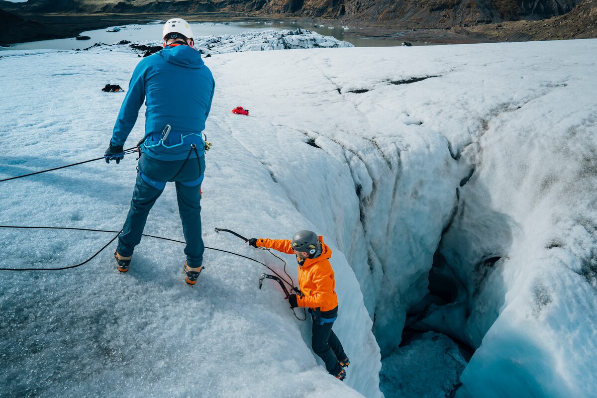 Tour guide assisting ice climber on Solheimajokull glacier steep glacier ice wall.
