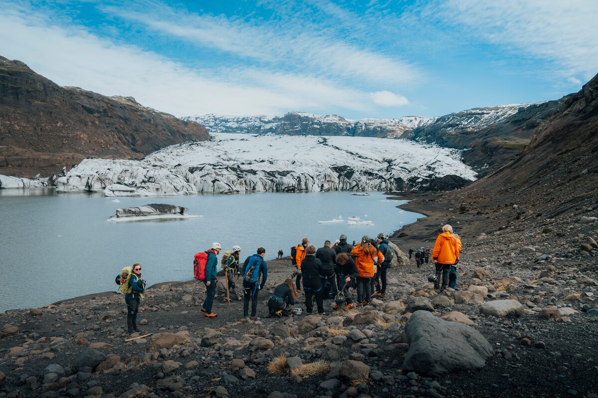 Small tour group standing at Solheimajokull glacier lagoon looking up towards glacier.