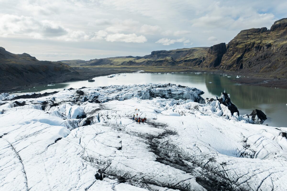 Aerial view of Solheimajokull glacier, small group walking across spring landscape.