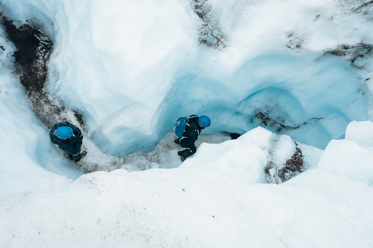Two glacier hikers walking through blue colored ice crevasse on Falljokull glacier.
