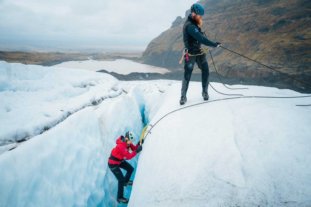 Ice climbing steep ice crevasse at Falljokull with view down from glacier to mountains.
