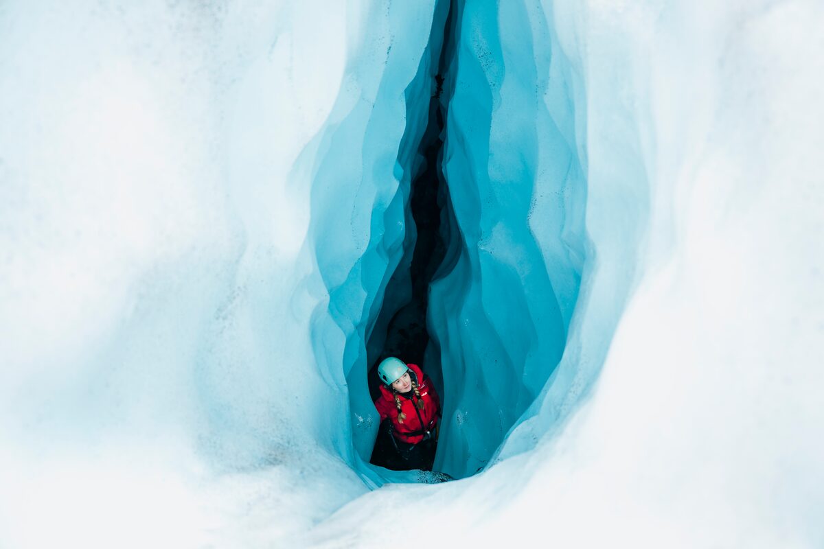 Tourist posing for photo stadning inside deep blue ice crevasse on glacier.