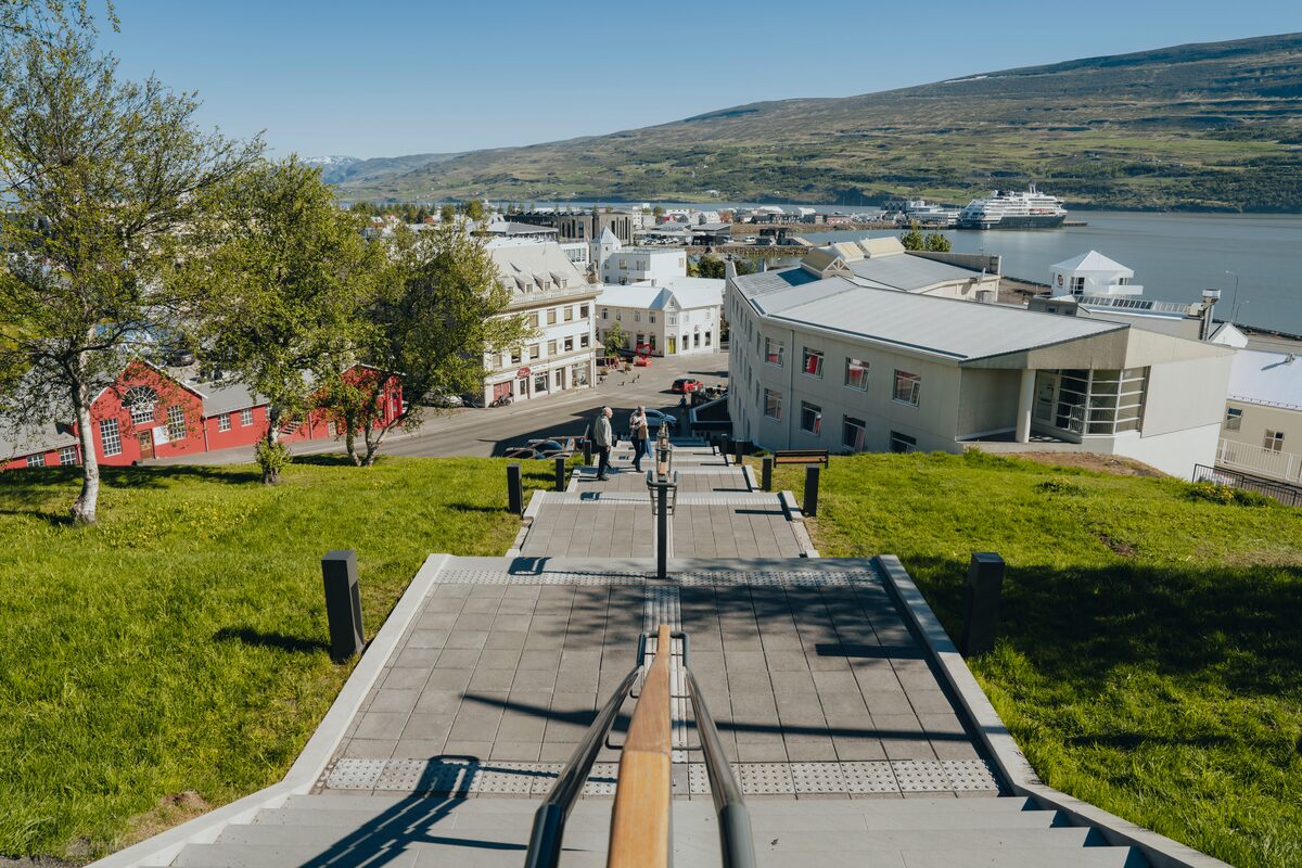 Down steps view to Akureyri old town, historic buildings with a view of harbor with whale watching boats in the distance.