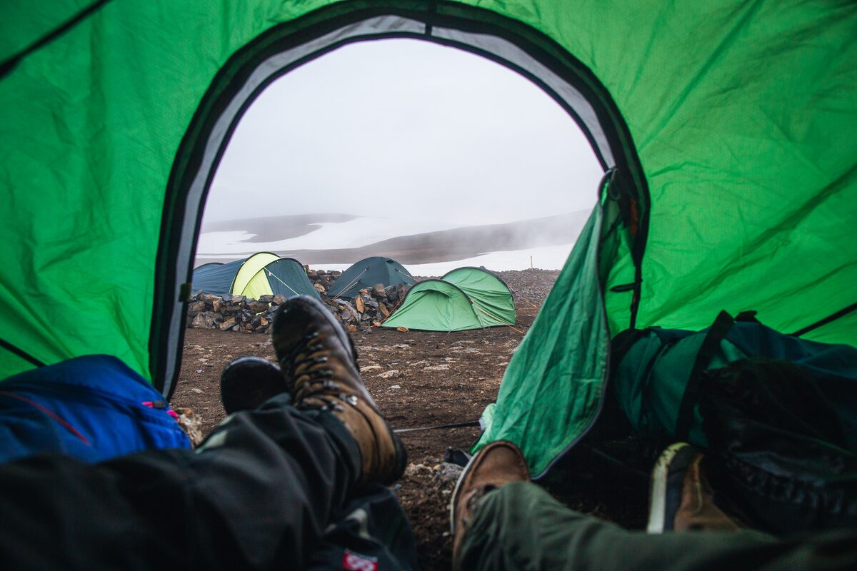 View from inside tent of legs crossed wearing hiking boots, at Landmannalaugar highlands.