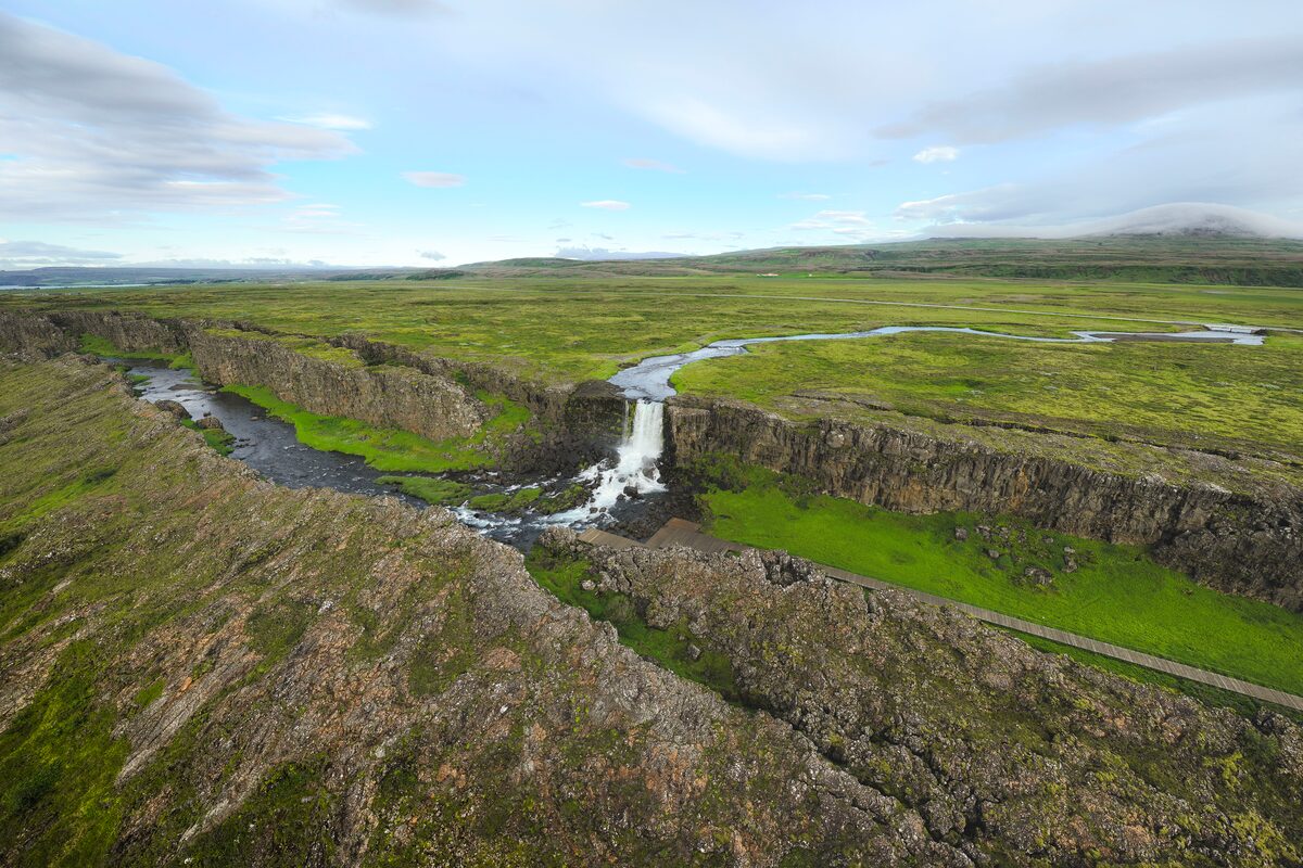 Waterfall at Thingvellir national park in between two tectonic plates with lushious green grass in summer.