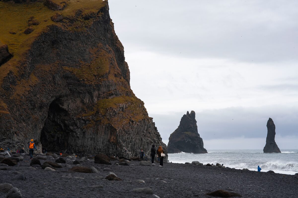 Few tourists walking on Reynisfjara black sand beach in autumn, by basalt sea stacks.