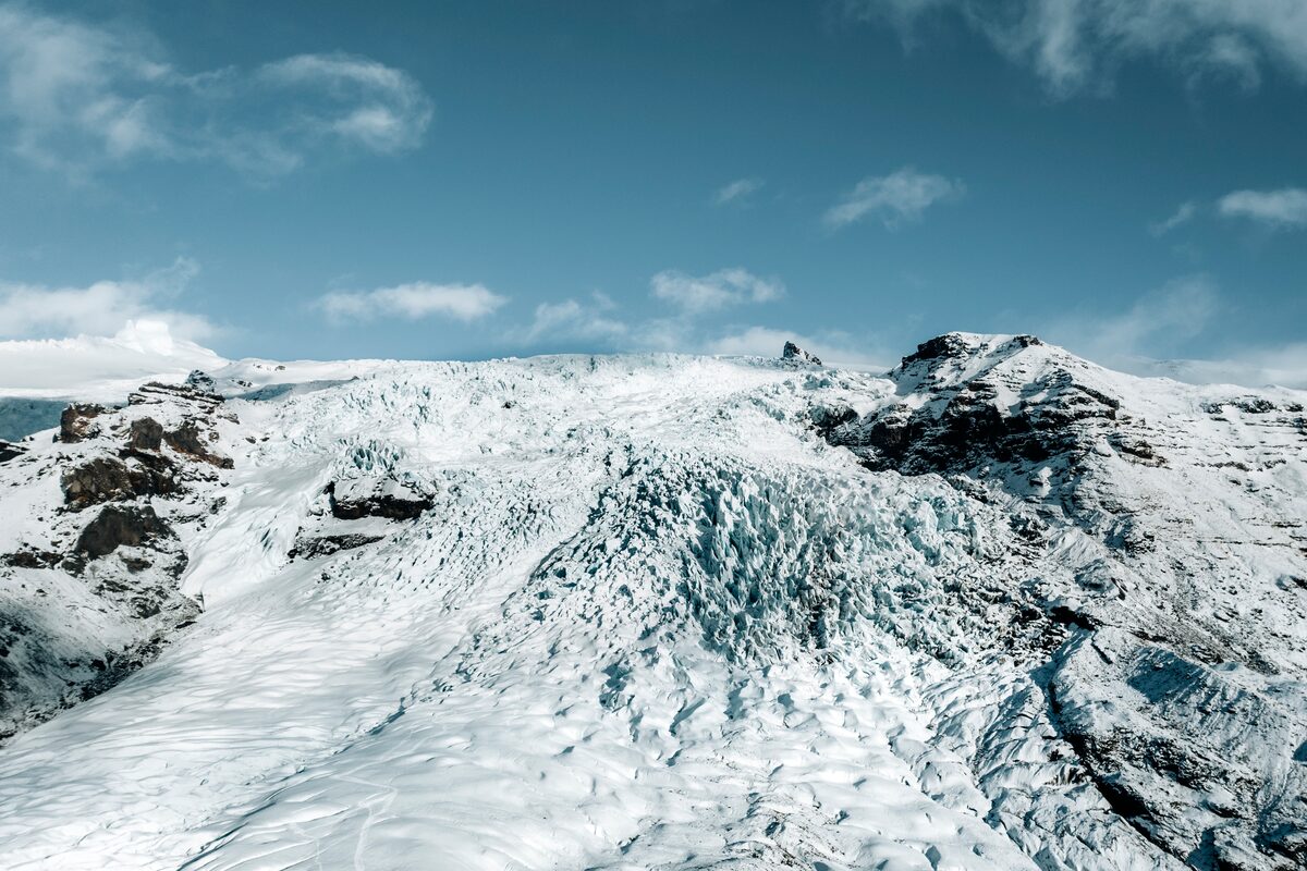 Wide shot view of Falljökull Glacier under clear blue skies, showcasing the glacier's rugged icy surface descending between steep mountain slopes.
