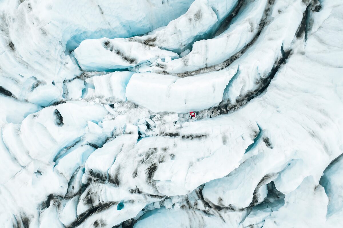 Bird’s eye view of a tourist navigating through a maze of blue ice crevasses on Falljökull Glacier in Iceland.