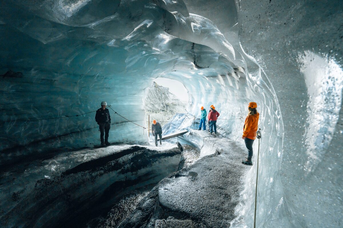 Small group of people exploring the interior of Katla ice cave, surrounded by blue and black reflecting ice walls.