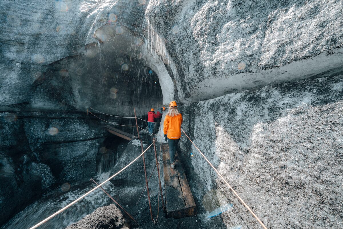 Wooden plank walking route along the volcano edge leading into Katla ice cave, surrounded by rugged volcanic terrain and icy cave entrance.