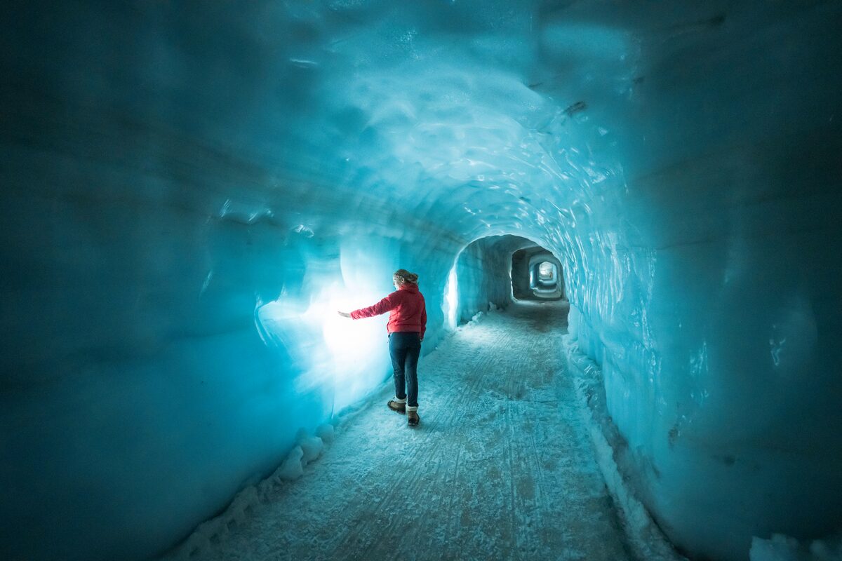 Female walking through Langjokull glacier famous ice tunnel, touching blue ice walls.