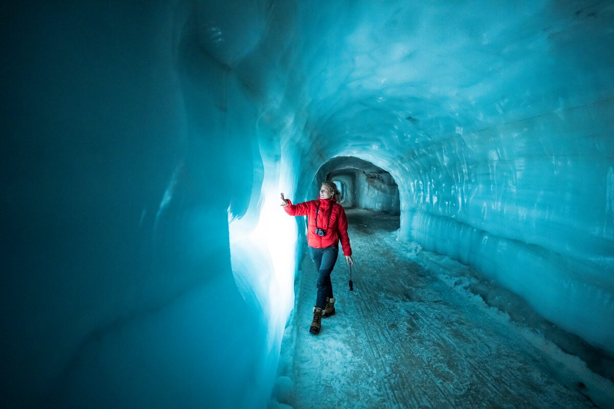 Female tourist touching blue ice tunnel wall at Langjokull glacier.