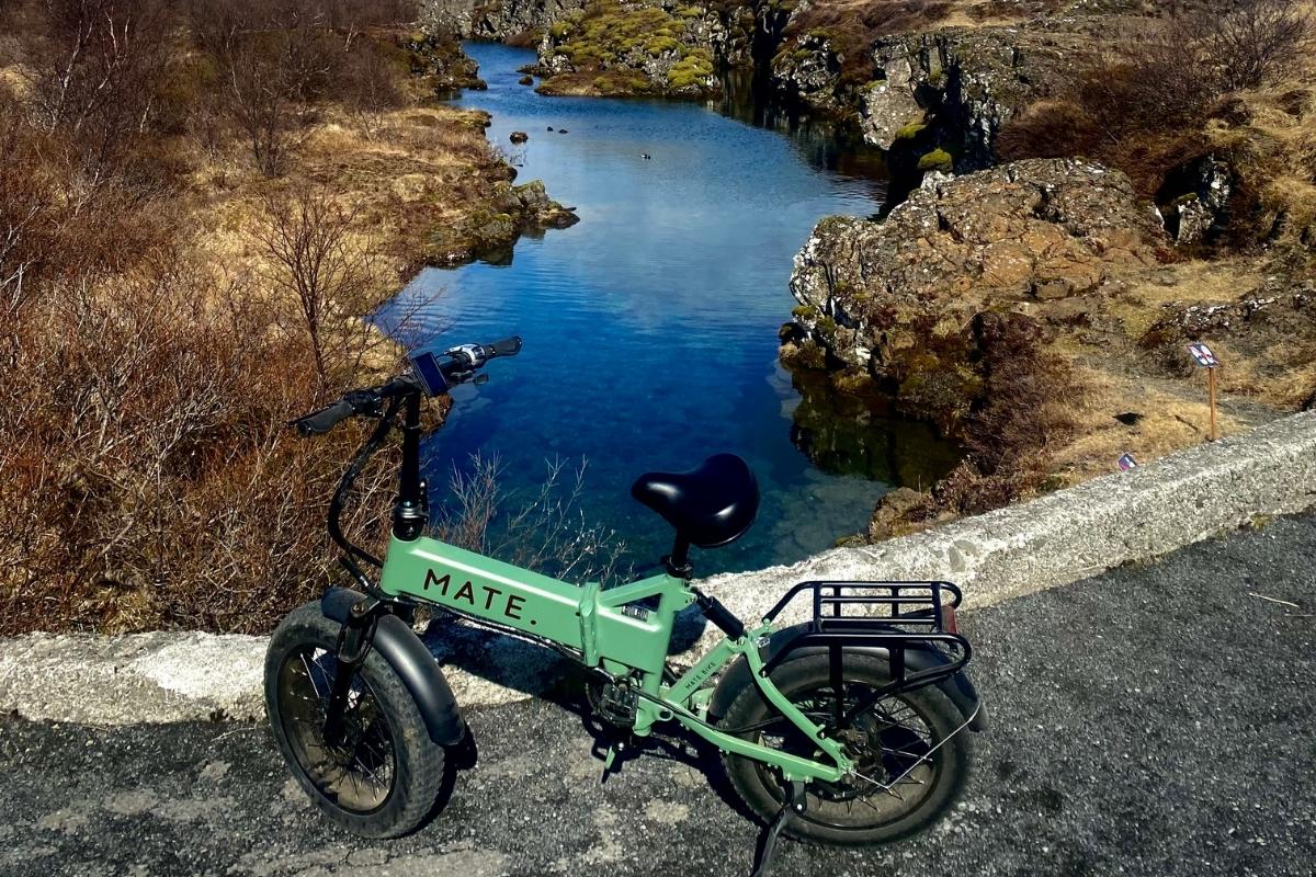 Green small electric bike parked by river in wild Reykjavik.