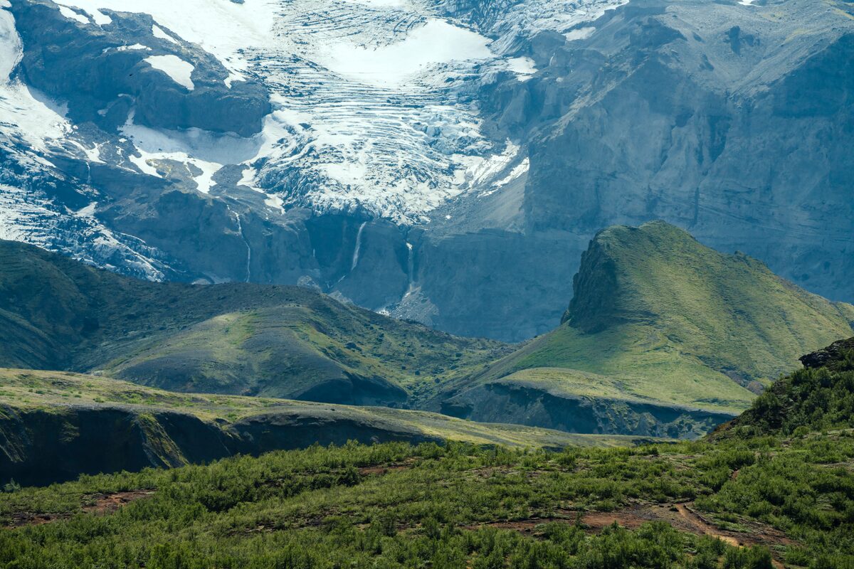 Scenic mountain views in Þórsmörk, Iceland, during summer, with rugged green peaks, distant snow-capped mountains.