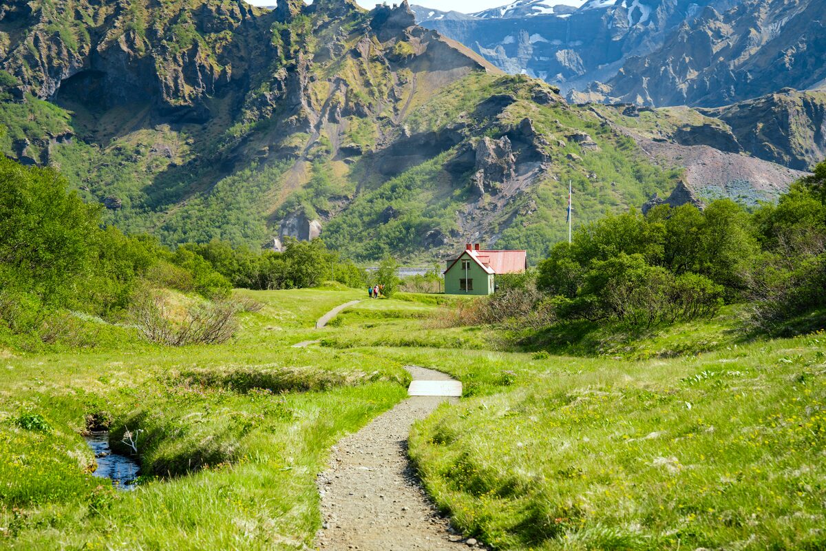 Thorsmork Base Hut nestled among lush green vegetation, surrounded by steep, moss-covered mountains under a partly cloudy summer sky in Iceland.