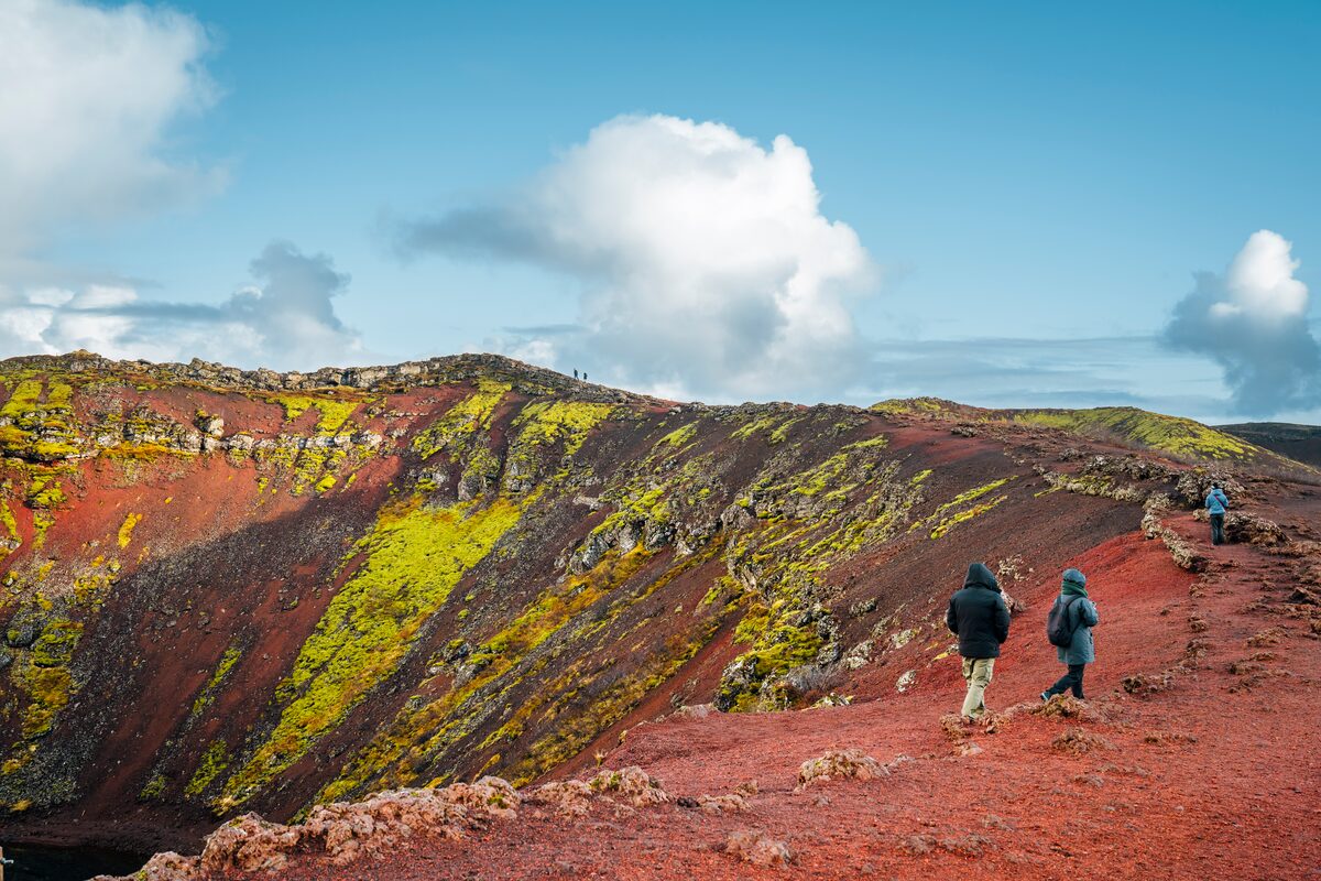 Tourists walking the red volcanic ash floor around Kerid on a blue summers day.