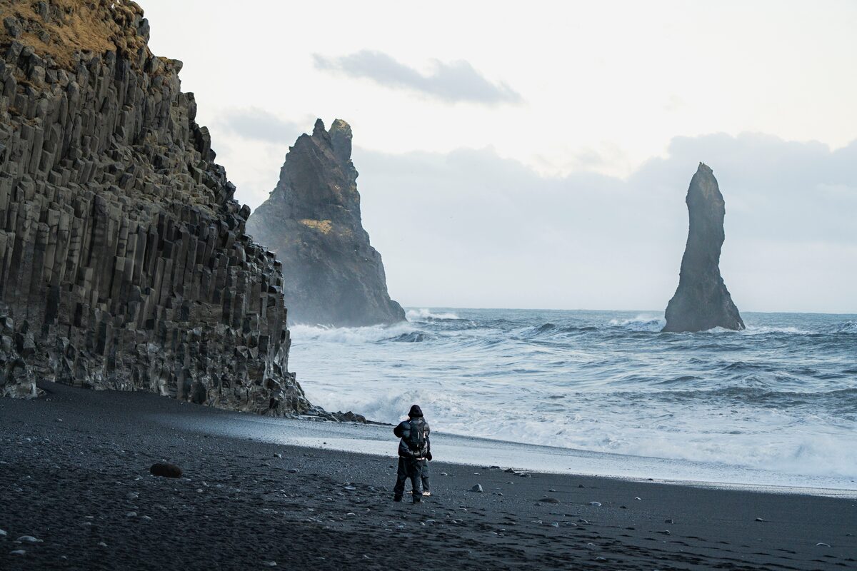 Tourists taking photos on Reynisfjara black sand beach with basalt columns and ocean waves in the background.